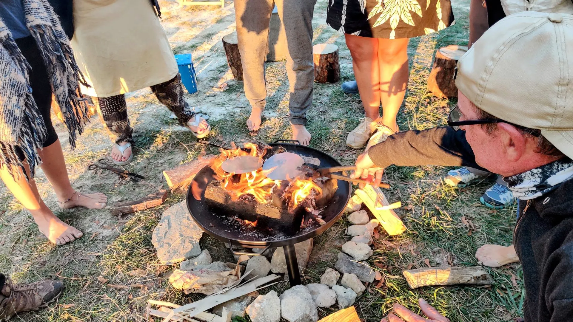 People gathered barefoot around a fire pit as metal discs are heated in the flames